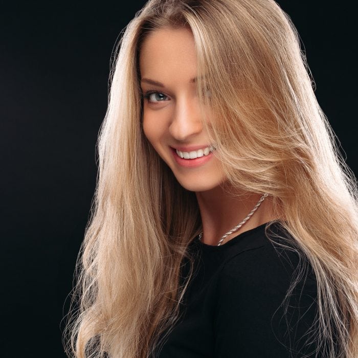 Studio portrait of happy beautiful girl with posing in studio on black background and smiling at camera. Beautiful model wearing black with perfect makeup after salon. Concept of beauty.